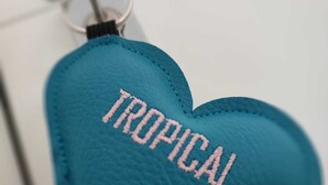 Un llavero azul en forma de corazón con la palabra 'TROPICAL' bordada.