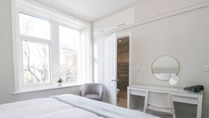 A bedroom with a large bed, a desk, a chair, and a walk-in closet. - Rocklands (Penrith)
