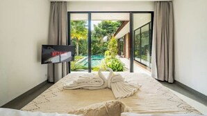 Ein modernes Hotelzimmer mit einem großen Bett, einem Flachbildfernseher und Blick auf einen Swimmingpool und Grünflächen.