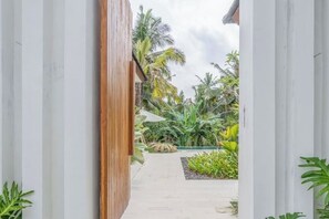 A pathway leading to a building with a wooden facade and a garden with tropical plants. - Villa The Kayu by GORO (Kabupaten Gianyar)