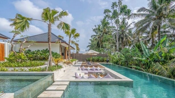 Ein Poolbereich mit klarem Wasser, umgeben von Palmen und einem Gebäude mit geneigtem Dach.