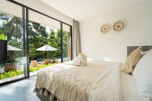 A modern hotel room with a large bed, a balcony with a view of lush greenery, and a glass wall. - Villa The Kayu by GORO (Kabupaten Gianyar)