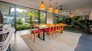 Ein moderner Essbereich mit Holztisch und Stühlen, großen Fenstern und hängenden Pendelleuchten.