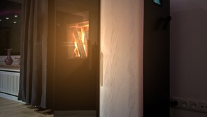 Ein moderner, kompakter Holzofen mit digitaler Anzeige, platziert in einer Ecke eines Raumes mit dunklem Boden und hellen Wänden.