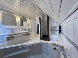Un baño moderno con una bañera grande, un tocador con espejo y una zona de ducha.