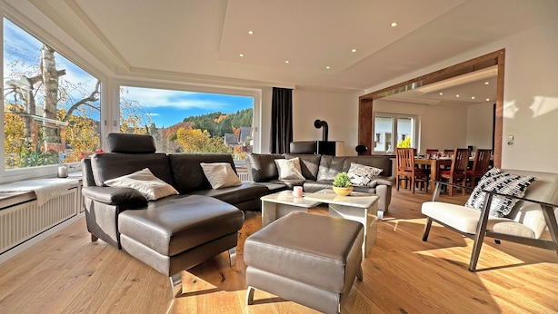 Ein modernes Wohnzimmer mit einem Ecksofa, einem Couchtisch und einem Essbereich im Hintergrund.