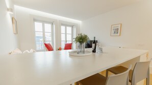 Eine moderne Küche mit weißer Arbeitsplatte, zwei Fenstern, einer Vase mit Grünpflanzen, einer Flasche und einem Weinglas.