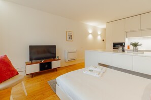 Una habitación de hotel moderna con cama, televisión, kitchenette pequeño y almohada roja.