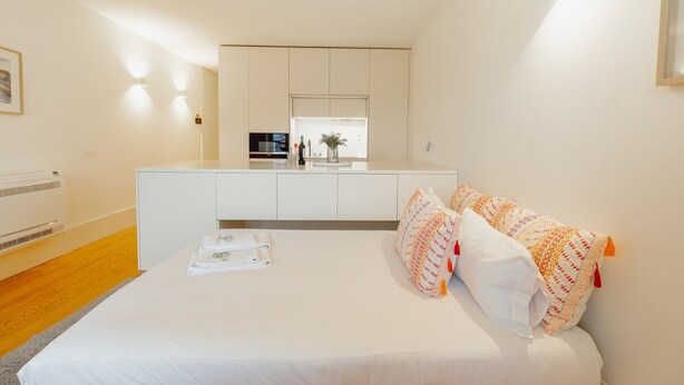 Ein modernes Hotelzimmer mit Bett, einer kleinen Küchenzeile und Blick auf die Stadtlandschaft.