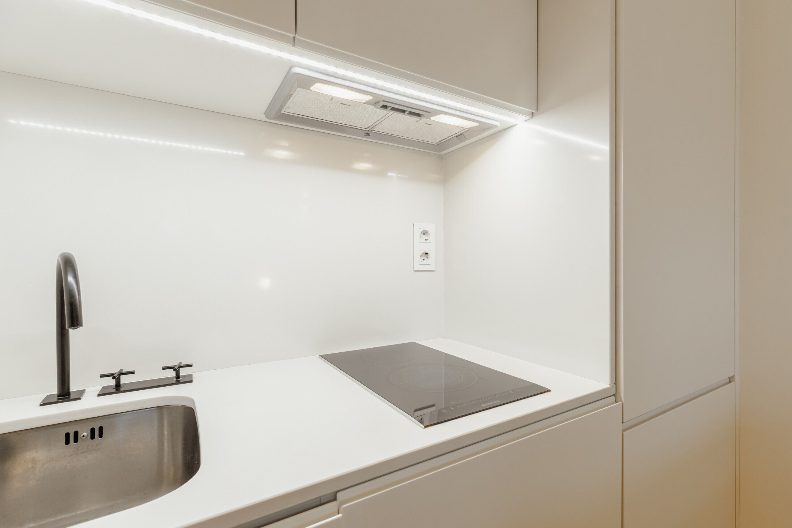 A modern kitchen with a stainless steel sink, a black induction cooktop, and white cabinetry.