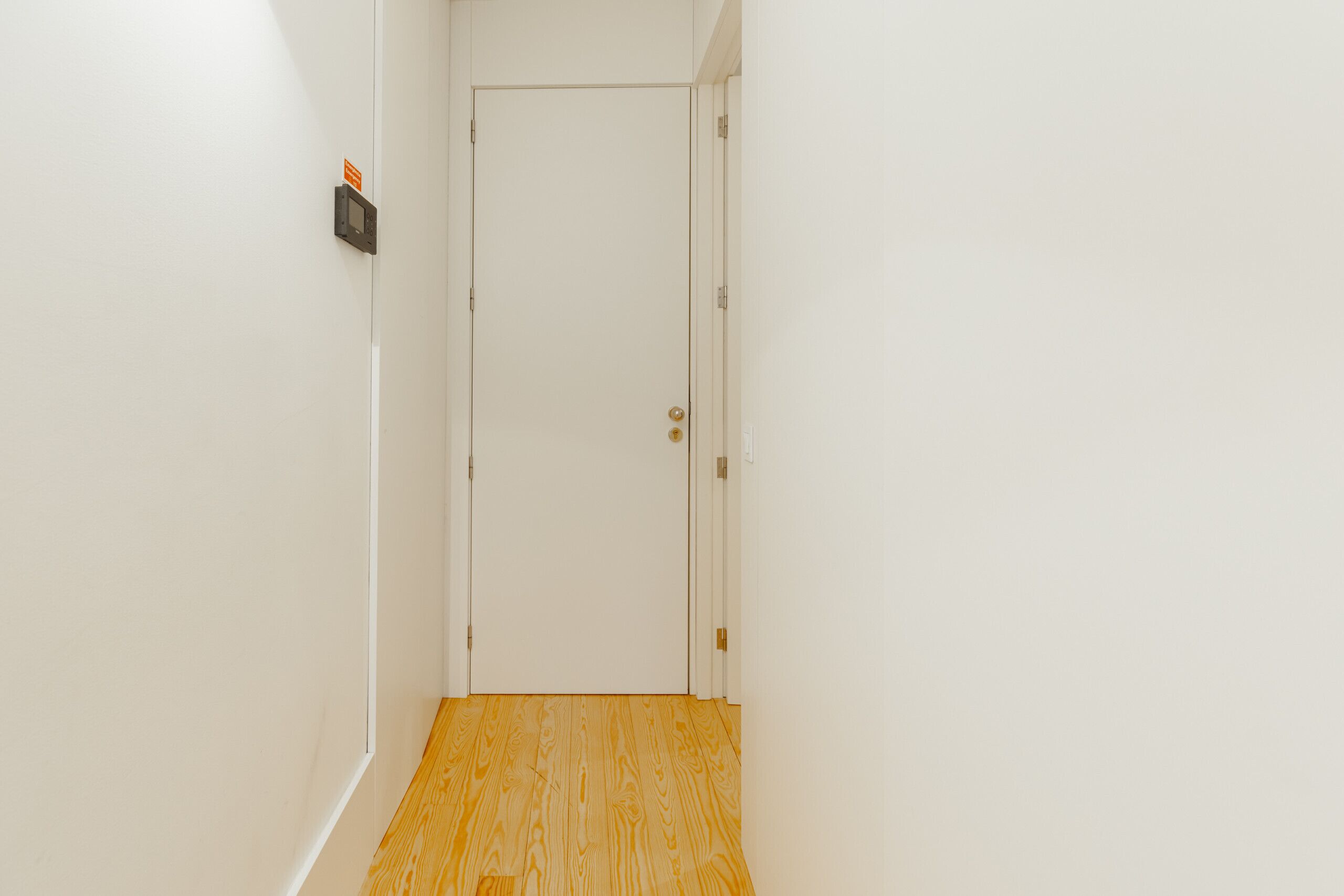 Un pasillo con piso de madera que conduce a una puerta blanca con un letrero en la pared.