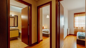 A hotel room with wooden flooring, a bed, a bedside table, a window with curtains, and a bathroom with a mirror and sink. - Downtown Deluxe 3 by Vacationy (Porto)