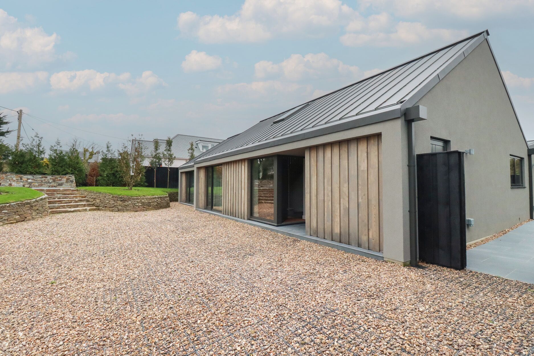 A modern building with a sloped roof, large windows, and a gravel driveway.