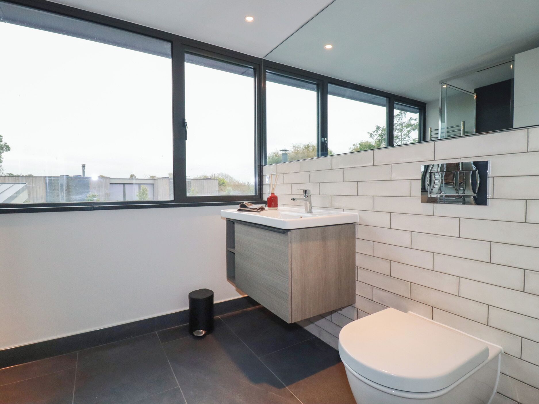 A modern bathroom with a large window, a sink, and a toilet.
