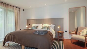 A modern bedroom with a large bed, a bedside table with a lamp, a chair, and a large mirror.