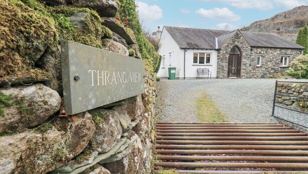 A stone wall with a sign reading "Thrang View" and a rustic building with a stone facade and a metal gate. - Thrang View (Ambleside)