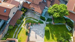 Ett flygbildsbild av ett bostadsområde med tak belagda med terrakottafärgade tegelpannor, en central innergård med en fontän och omgivande grönska.