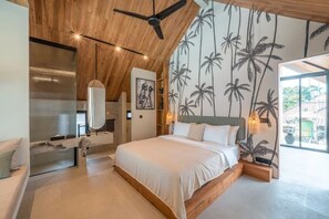 A bedroom with a wooden ceiling, a bed with white bedding, a large mirror, and a wall with palm tree wallpaper. - Villa Bayu by GORO (Bali)