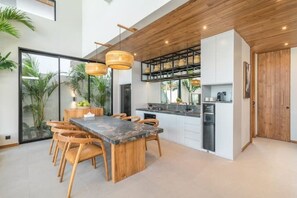 A modern kitchen with a central island, wooden chairs, and pendant lights. - Villa Bayu by GORO (Bali)