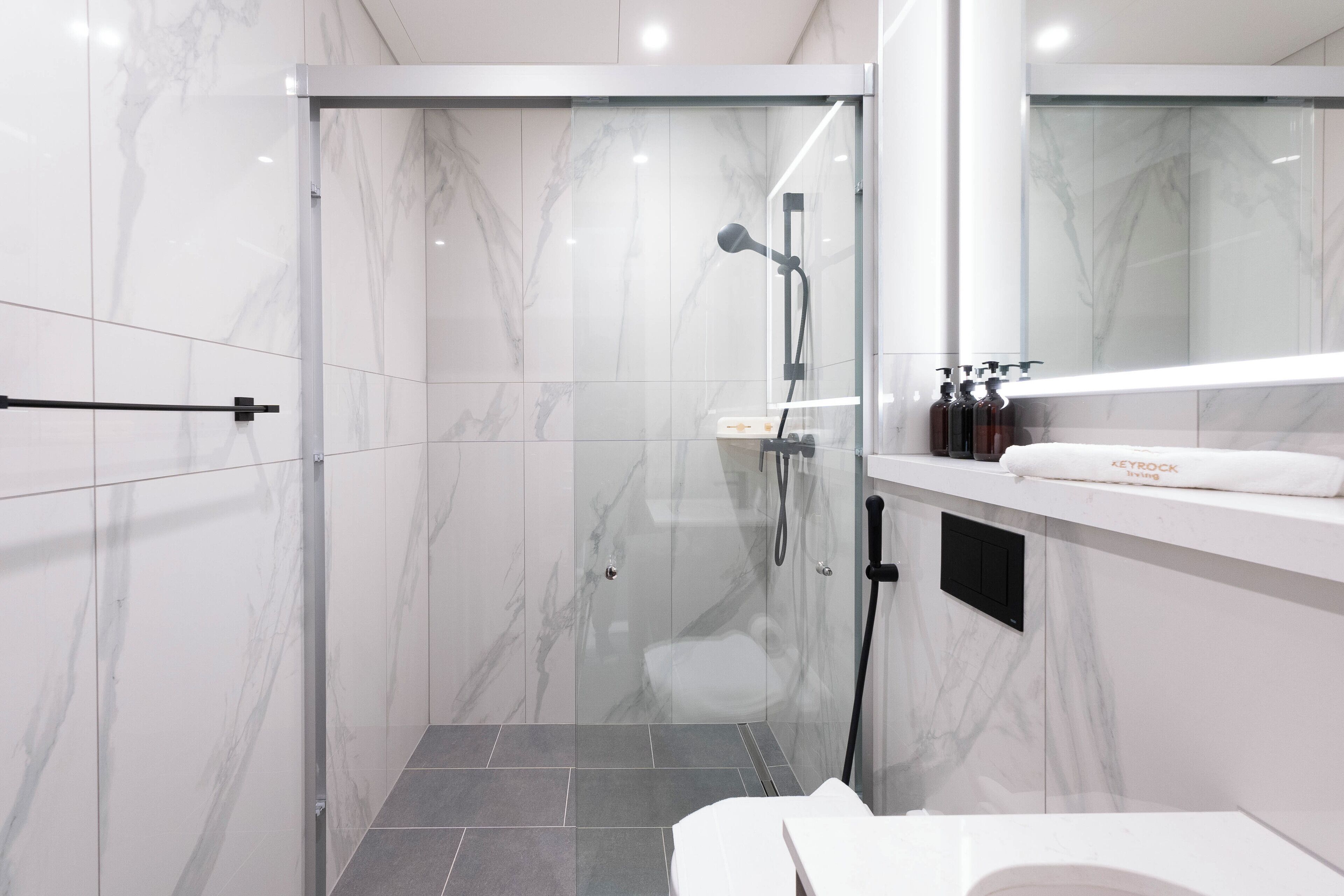 Ein modernes Badezimmer mit einer Glaskabine zur Dusche, Marmorwänden und einem weißen Waschbecken mit Handtuch.