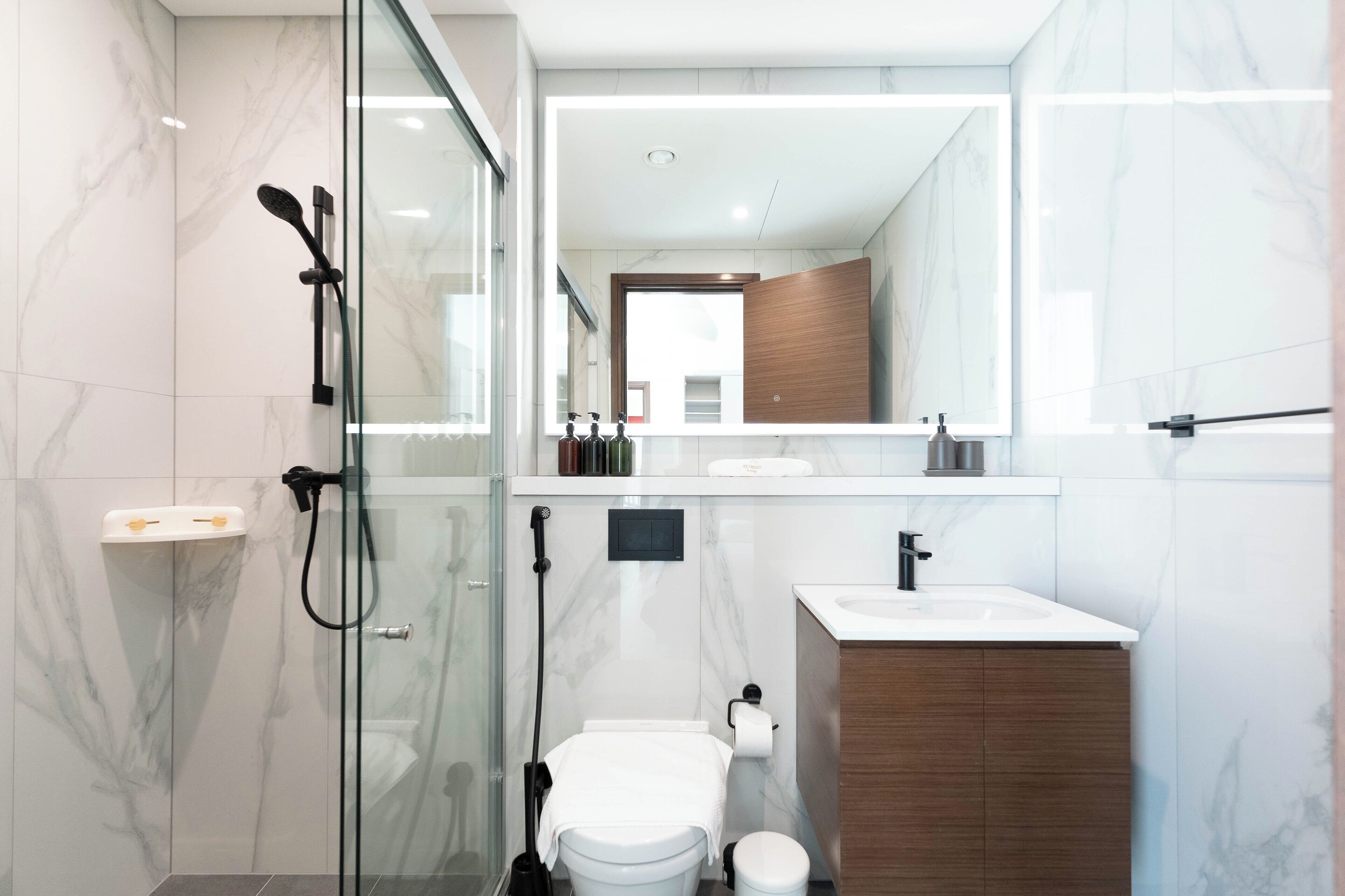 A modern bathroom with a glass-enclosed shower, a toilet, and a vanity with a mirror.