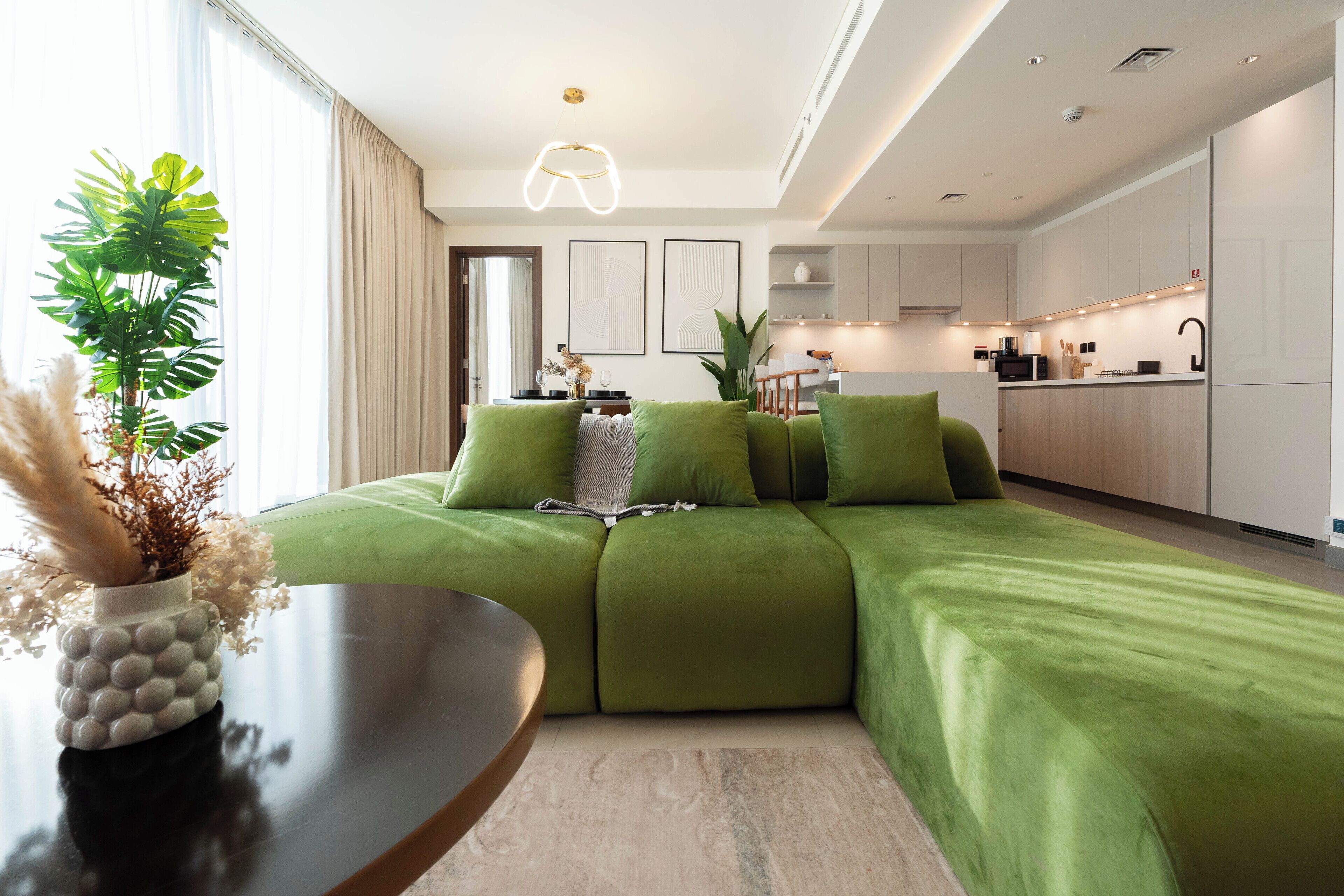 Un salon moderne avec un canapé d’angle vert, une table ronde en bois et une plante en pot.