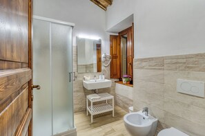 Ein Badezimmer mit Holztür, Waschbecken in Weiß, einem Spiegel und einem Bidet.