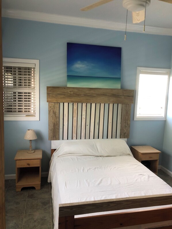 A bedroom with a wooden headboard, a bed with white bedding, a nightstand with a lamp, and a window with blinds. - The Blue House,Oceanfront with 4 bedrooms 2 bath sleeps 10 in beds, water access (Spanish Wells)