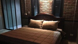 A bed with a brown quilt and two pillows, a wooden headboard, and a brick wall with a window. - Room-peaceful House Surrounding by Natur (Ao Luek)