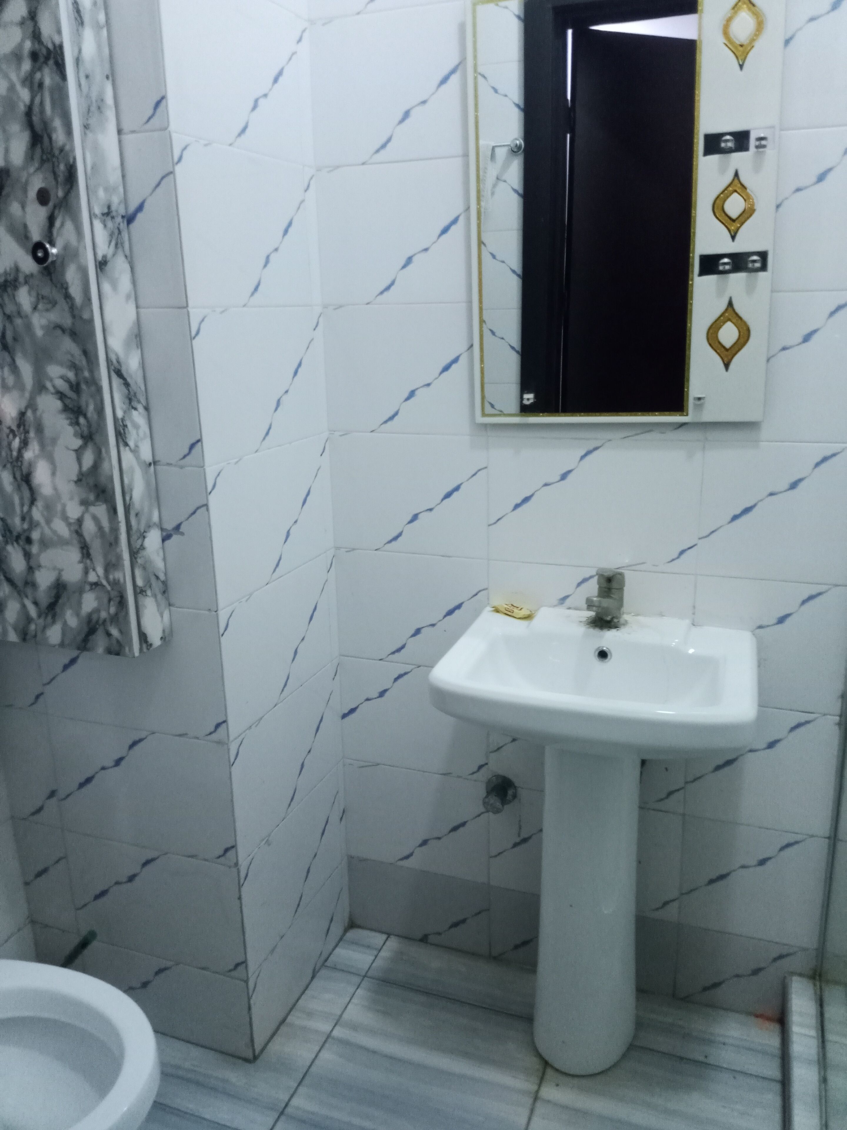 A bathroom with white marble tiles, a white sink, a mirror, and a toilet.