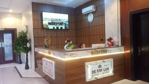 Egy recepciós pult, amelyen egy tábla található, rajta a felirattal: „DE BAY LUX HOTEL & SUITES”.