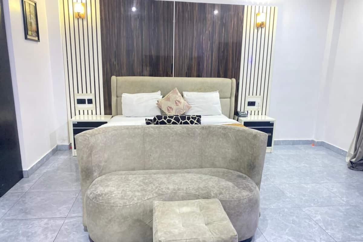 A modern bedroom with a curved sofa and ottoman, a large bed with multiple pillows, and a wall-mounted light fixture.