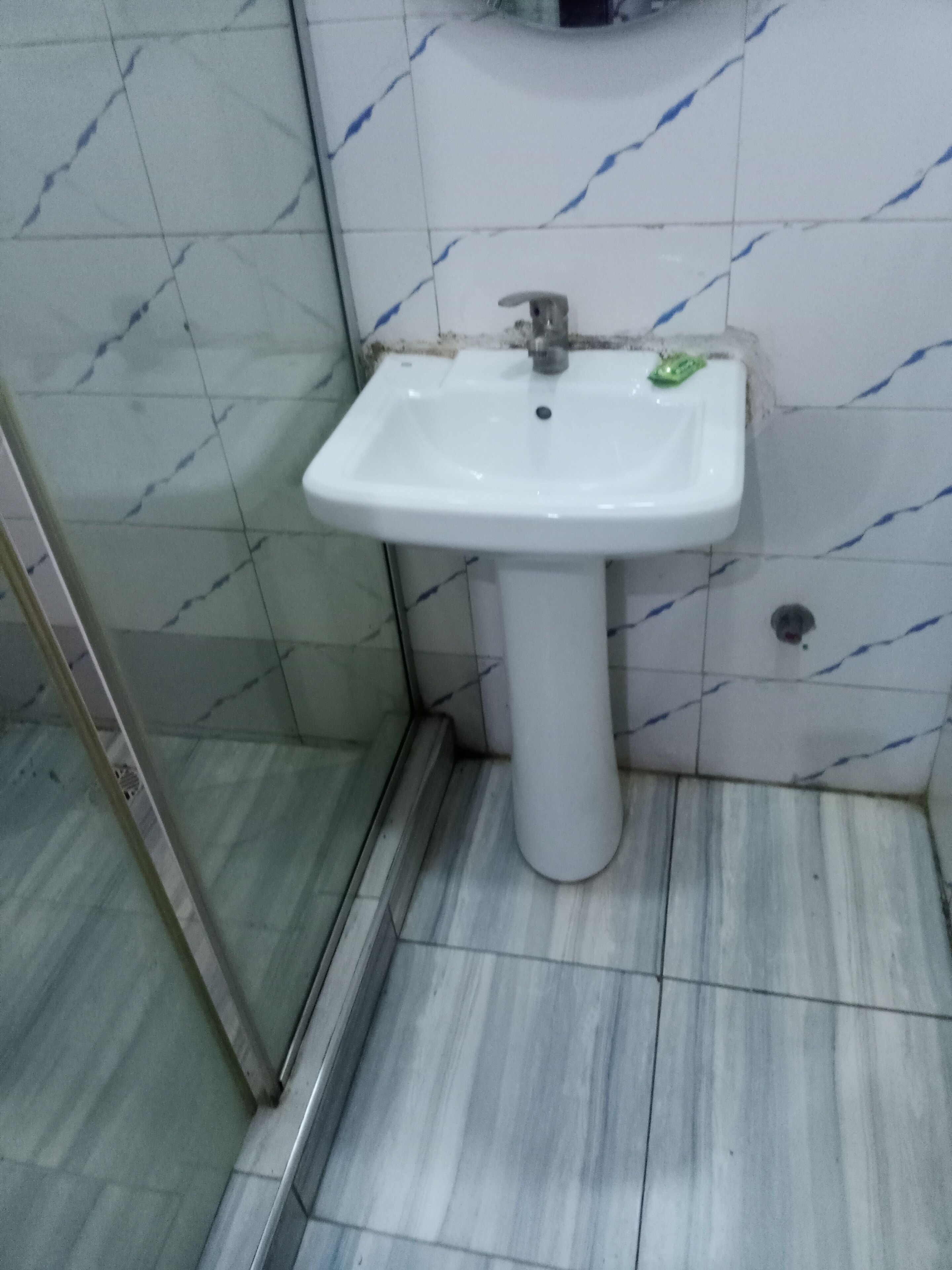 Un baño con un lavamanos blanco pedestal, una cabina de ducha de vidrio y suelo de baldosas.