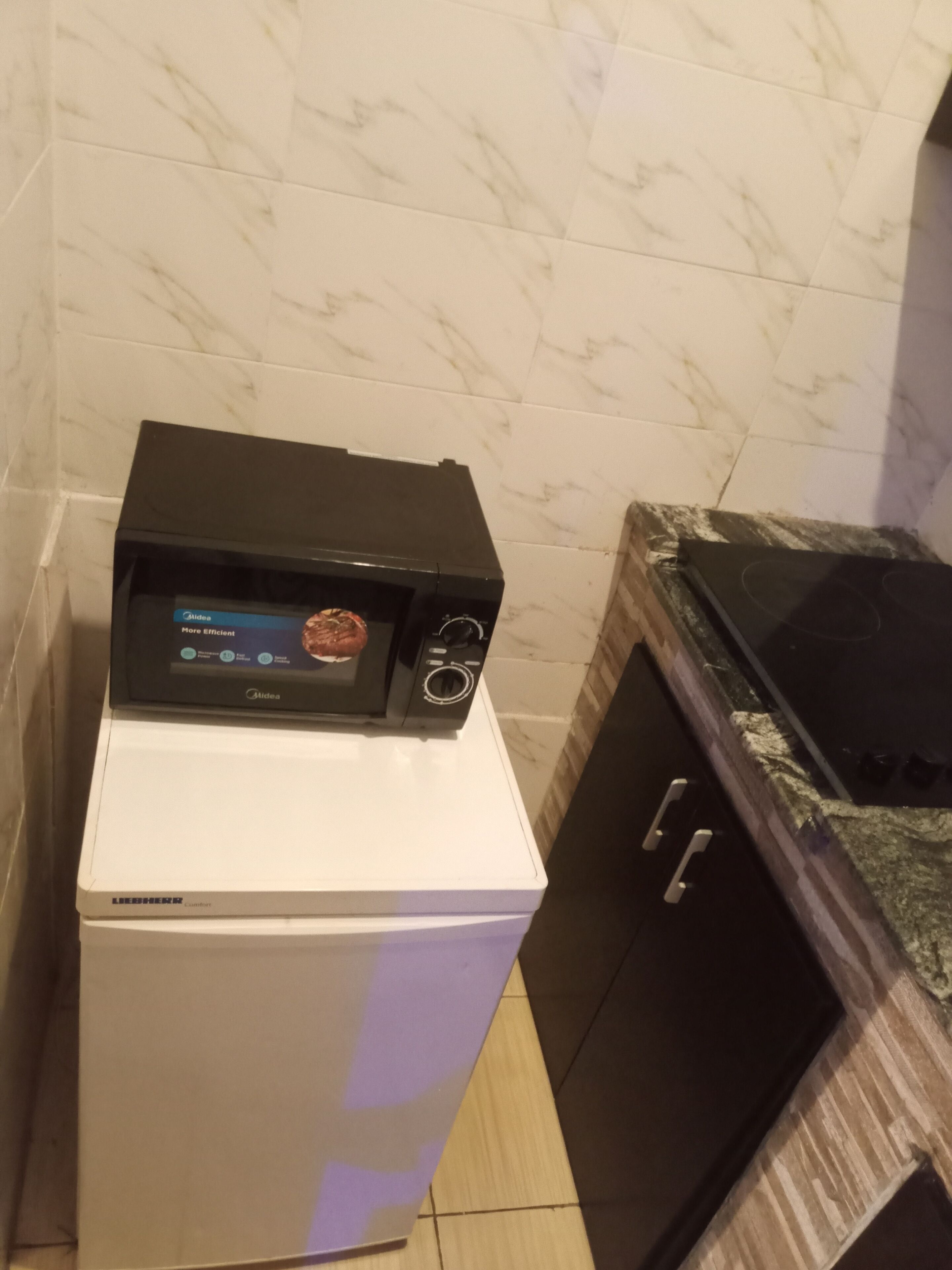 A compact kitchen with a microwave on top of a white refrigerator, a black oven, and a granite countertop.