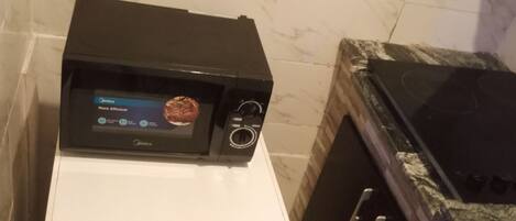 A compact kitchen with a microwave on top of a white refrigerator, a black oven, and a granite countertop.