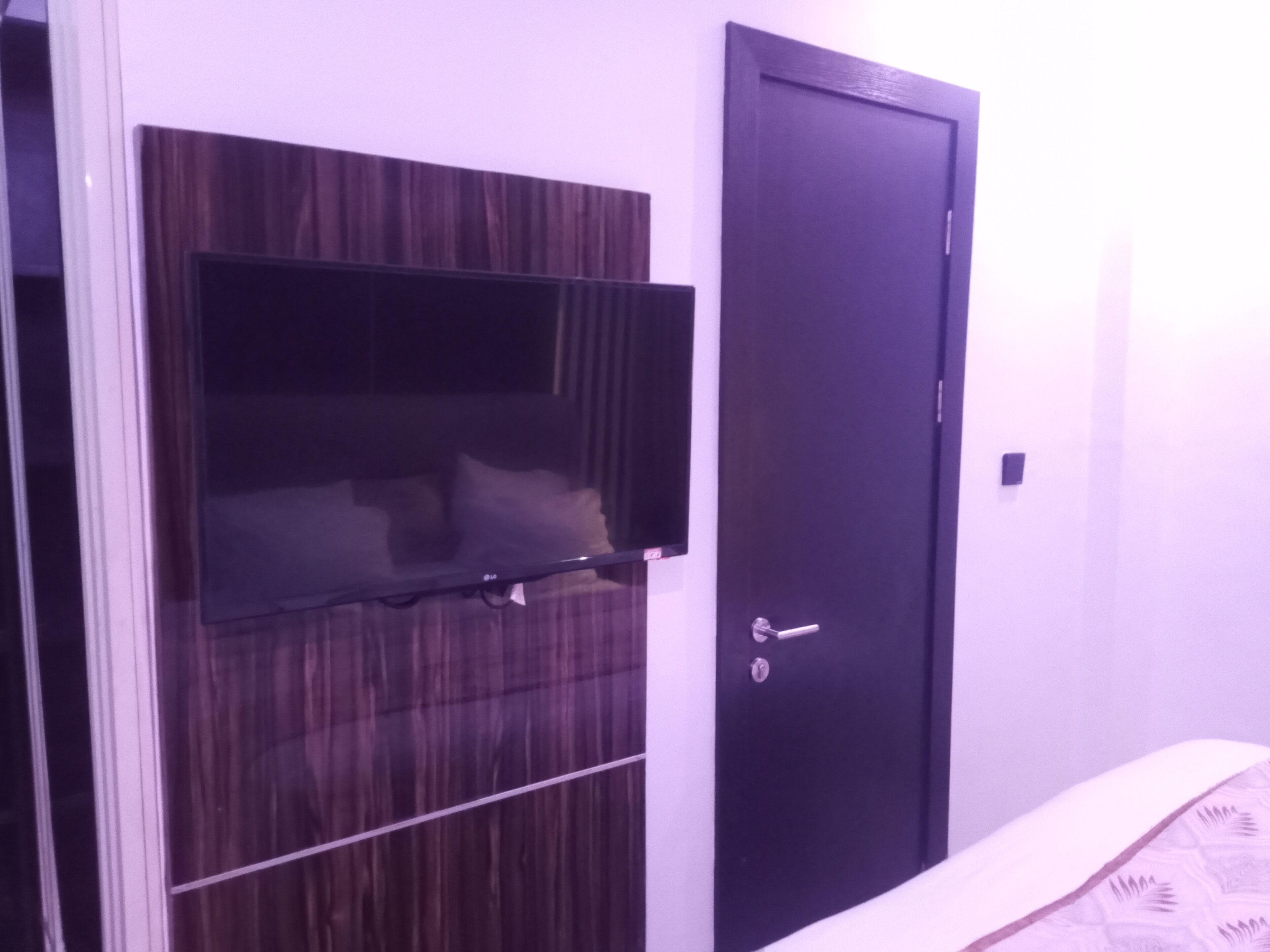 A room with a dark wooden wardrobe, a flat-screen TV mounted on it, and a closed door.