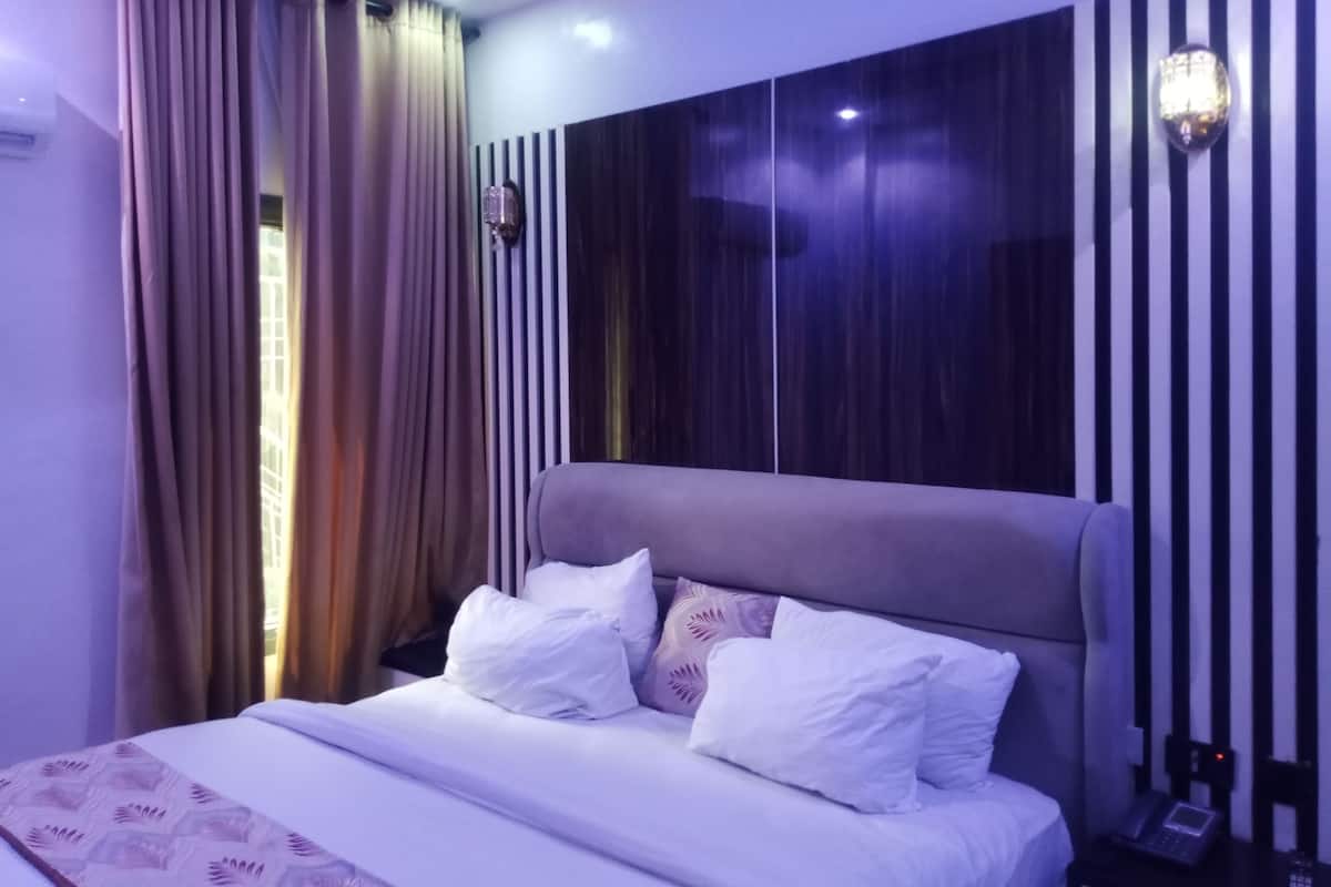 A modern bedroom with a large bed, a headboard, and a wall-mounted light fixture.