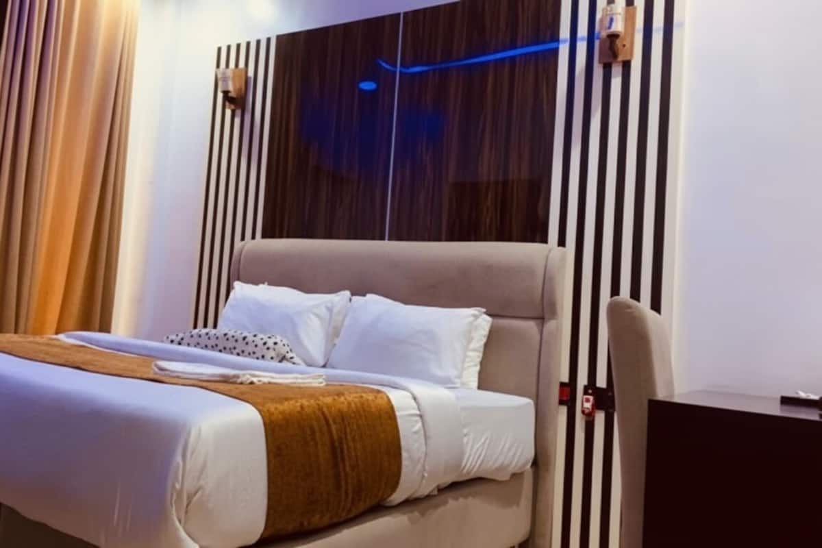 A modern hotel room with a large bed, a wooden headboard, and a curtain on the left.