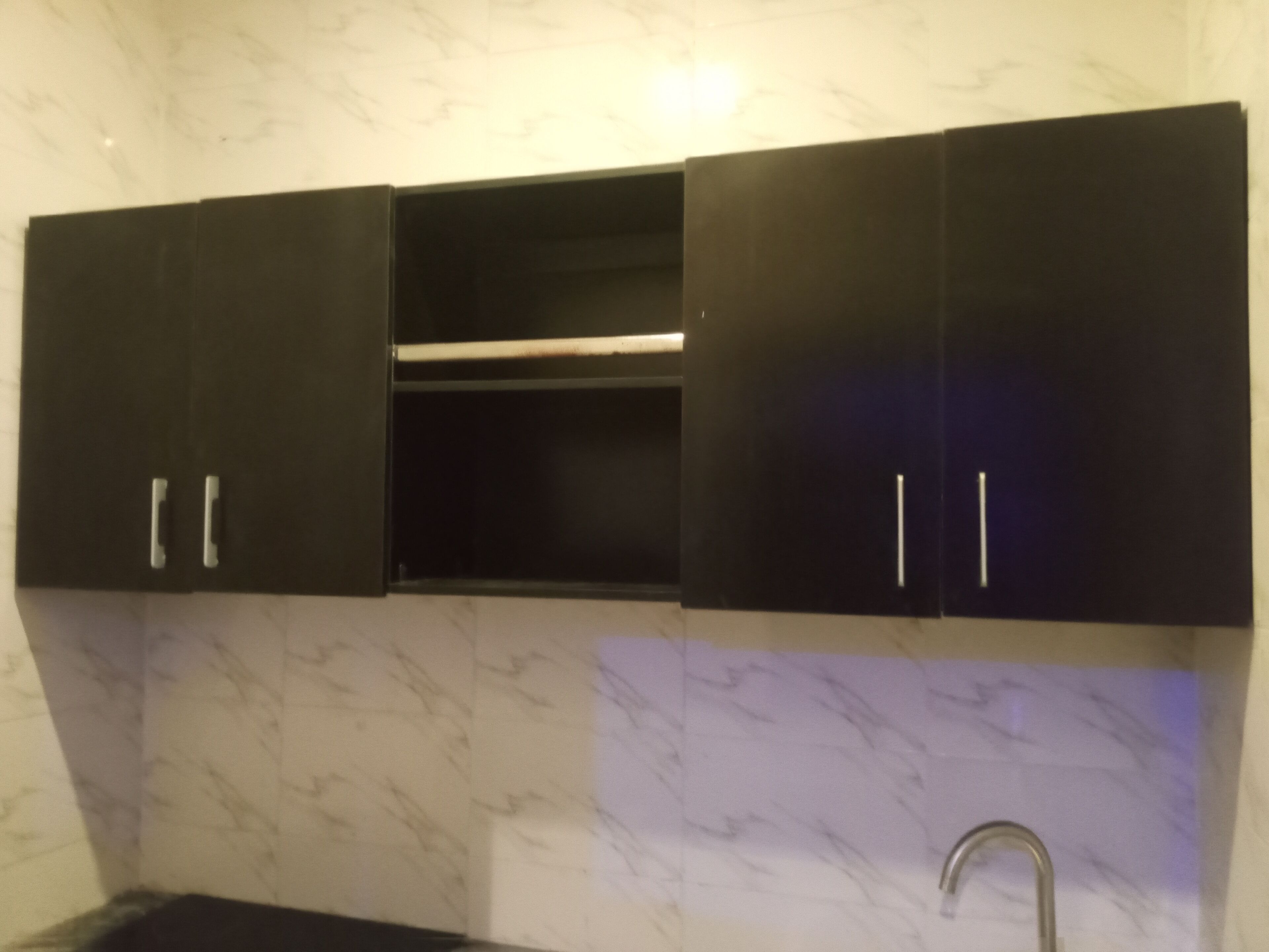 A kitchen with black cabinets, a marble backsplash, and a stainless steel sink.