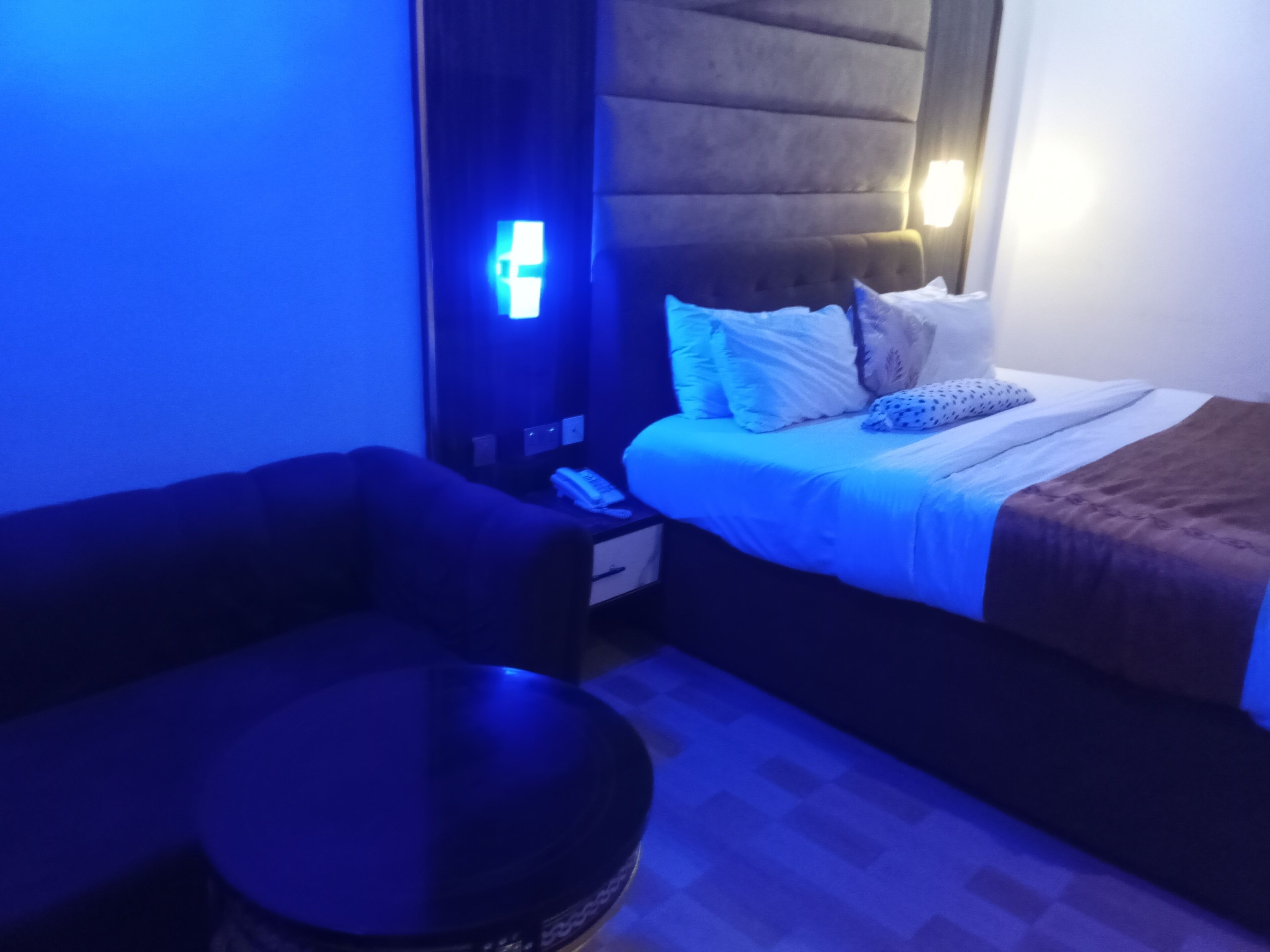 Ett hotellrum med en säng, ett nattduksbord med en telefon, ett litet runt bord och en väggmonterad lampa.