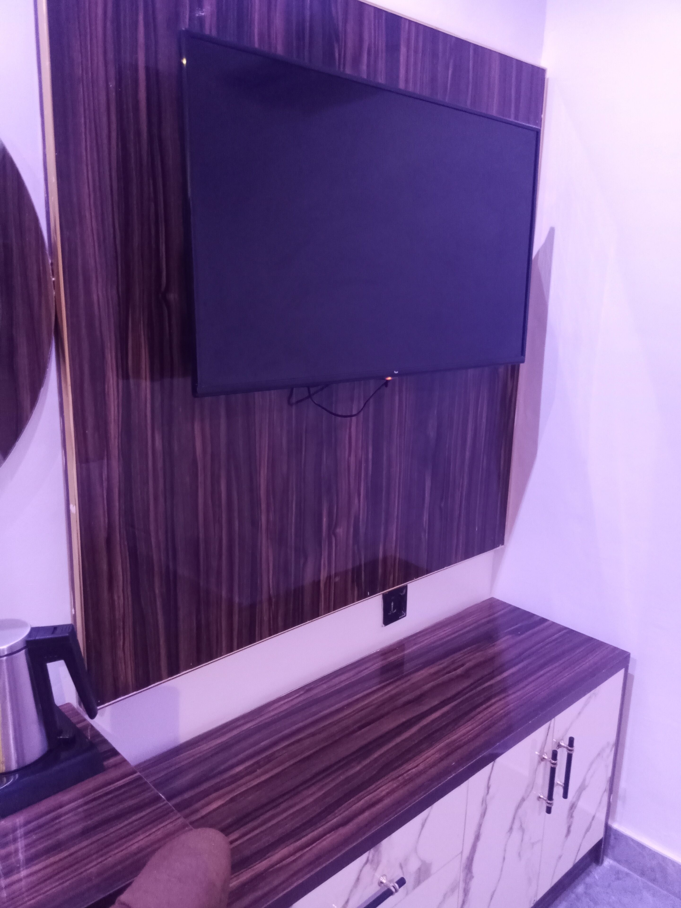 Un soggiorno moderno con una televisione a schermo piatto montata su una parete in legno, un mobiletto in legno scuro sottostante e un piccolo sgabello metallico a sinistra.