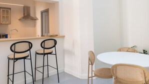 A compact kitchen with a built-in stove, a sink, and a window above the counter. There are two black bar stools and a round table with two wicker chairs. - Apartment RDC Arena Gare center (Reims)