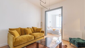 A modern living room with a mustard-colored sofa, a glass coffee table, and a green ottoman. - Apartment RDC Arena Gare center (Reims)