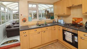 A kitchen with wooden cabinets, a gas stove, a sink, and a window overlooking a garden. - 5 Overstone Drive (Wisbech)