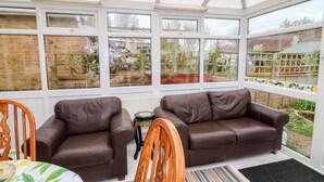 A conservatory with two brown leather sofas, a wooden chair, and a small table with a patterned tablecloth. - 5 Overstone Drive (Wisbech)