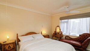 A bedroom with a large bed, a nightstand with a lamp, a dresser with a mirror, a leather armchair, and a ceiling fan. - 5 Overstone Drive (Wisbech)