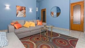 A living room with a grey sofa, orange and yellow cushions, a patterned rug, a round mirror, and a wooden door with a glass panel. - Apartment 'Lemon Terrace' with Private Terrace, Wi-Fi and Air Conditioning (Catania)