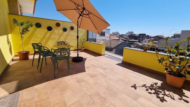 A rooftop terrace with yellow walls, a table with chairs, a potted plant, and a large umbrella. - Apartment 'Lemon Terrace' with Private Terrace, Wi-Fi and Air Conditioning (Catania)