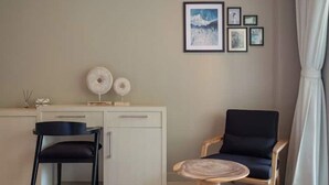 Ein Zimmer mit Schreibtisch, zwei Stühlen, einem kleinen runden Tisch und einer Wand mit gerahmten Bildern.
