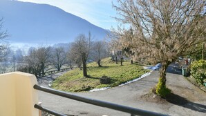 Una strada asfaltata con una ringhiera metallica, un'area verdeggiante con un albero e una montagna sullo sfondo.